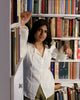 Model in library styling ivory string blouse with book in hand, showcasing airy summer fabric.