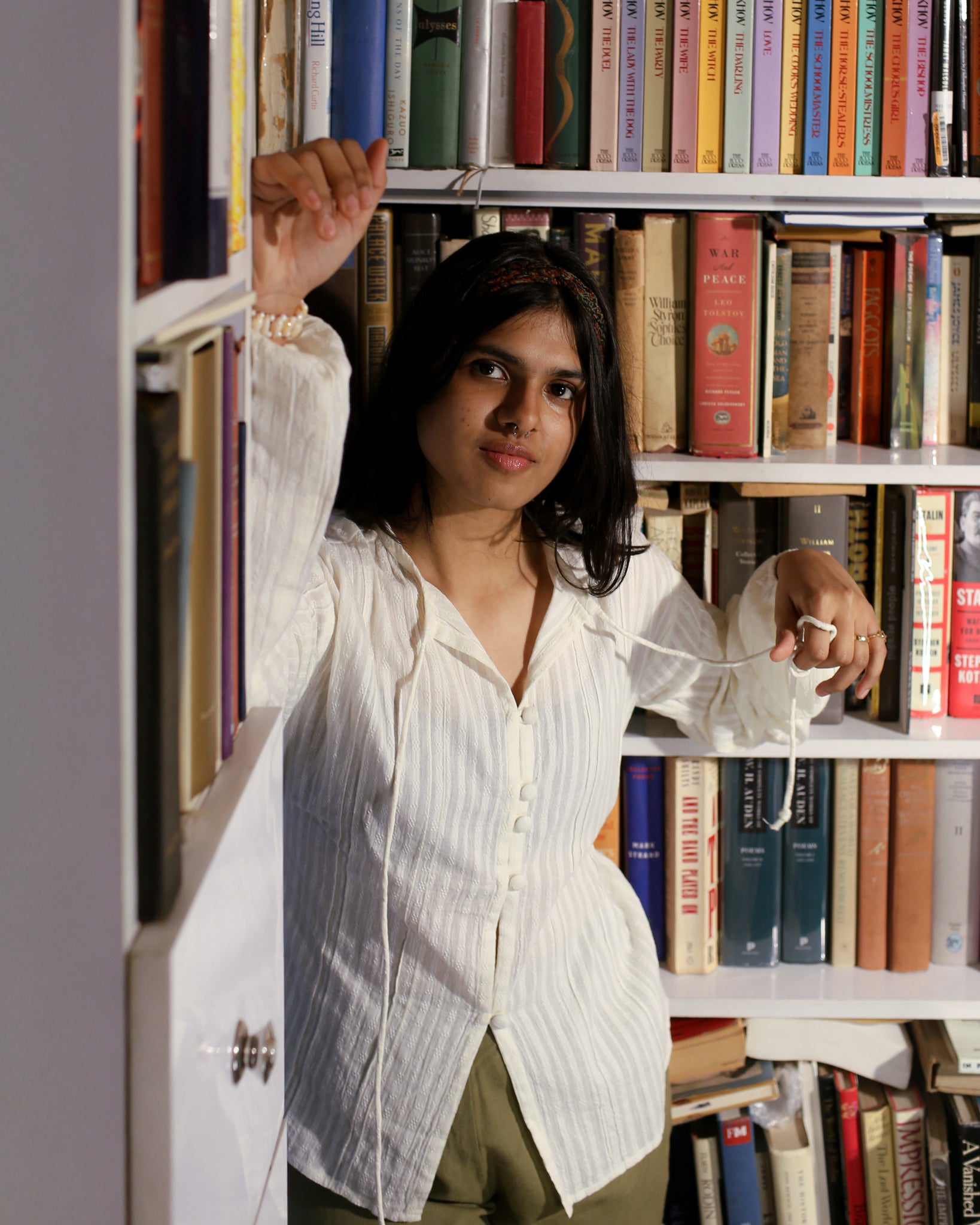 Model in library styling ivory string blouse with book in hand, showcasing airy summer fabric.