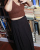Model wearing a black cotton skirt styled with a fitted brown woollen top in library.