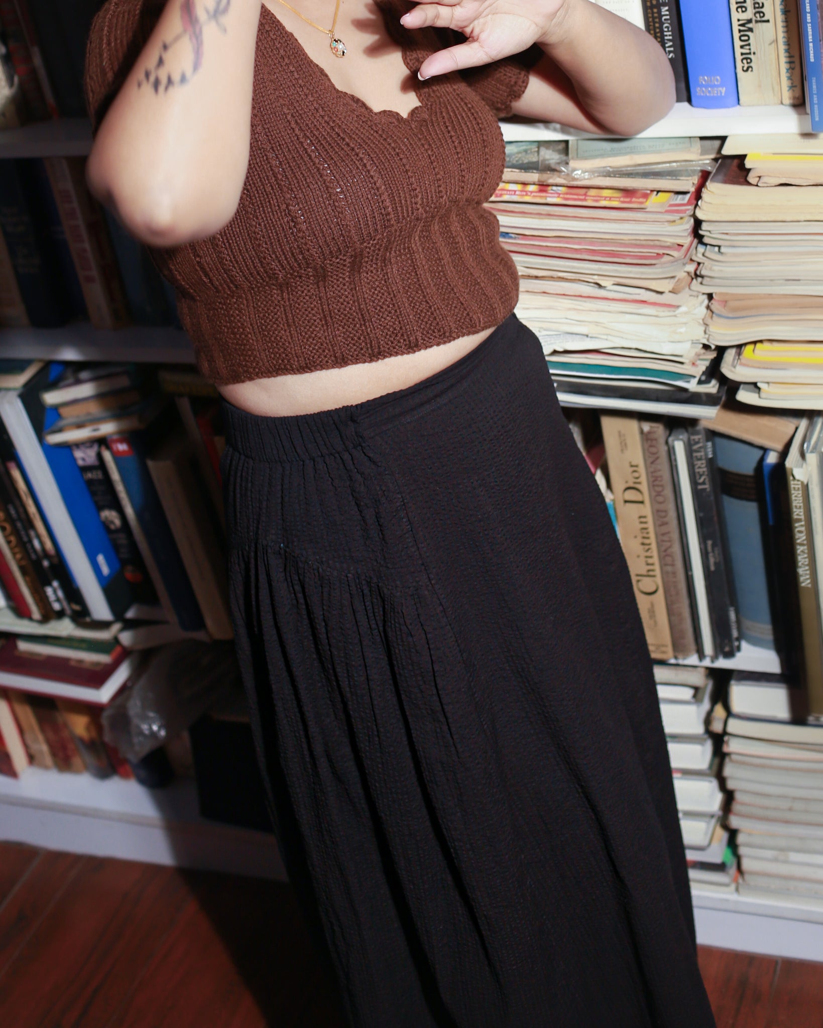 Model wearing a black cotton skirt styled with a fitted brown woollen top in library.