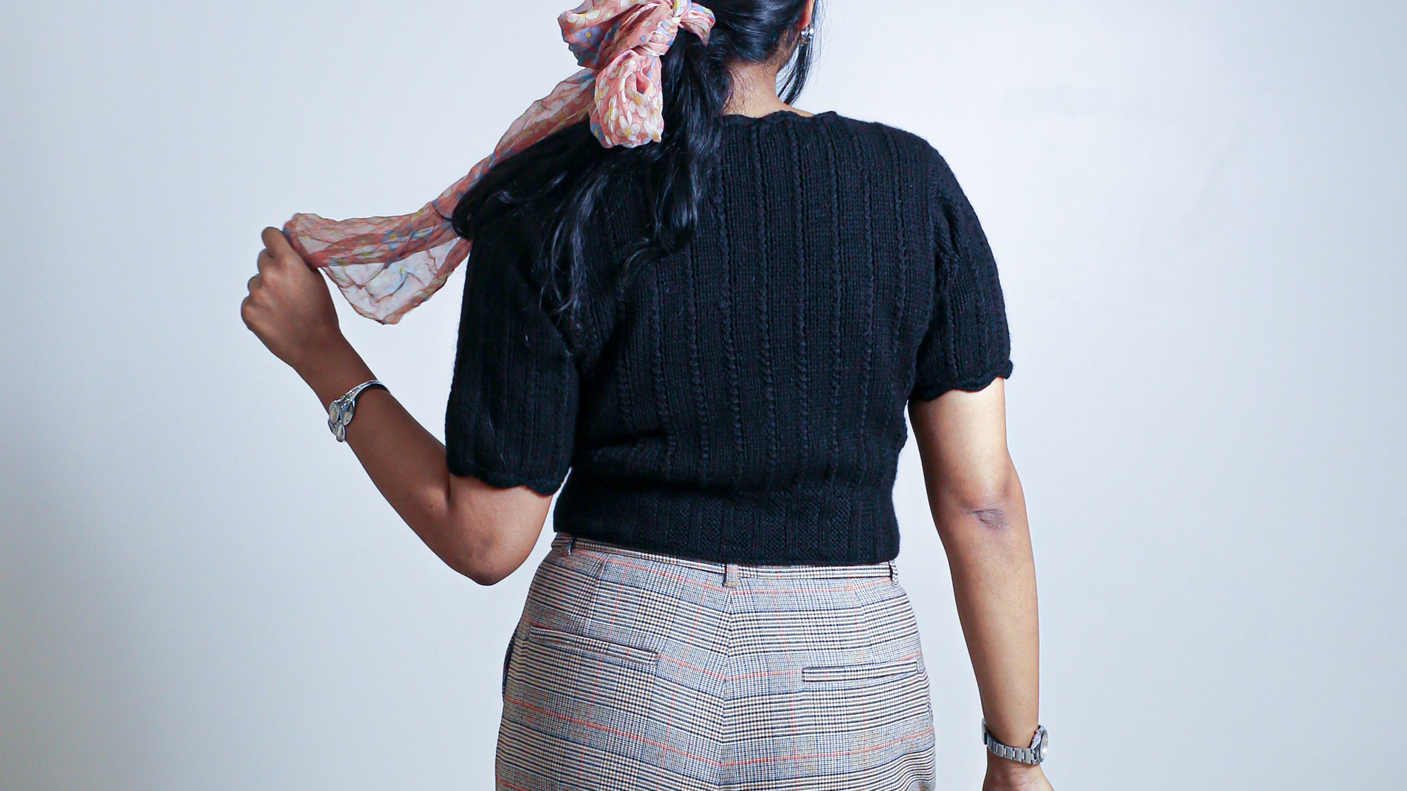Back view of a black scallop neck sweater in 100% pure wool styled with high-waisted trousers.
