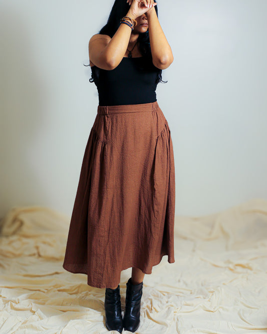 Model wearing a brown cotton skirt styled with a fitted black top and boots.