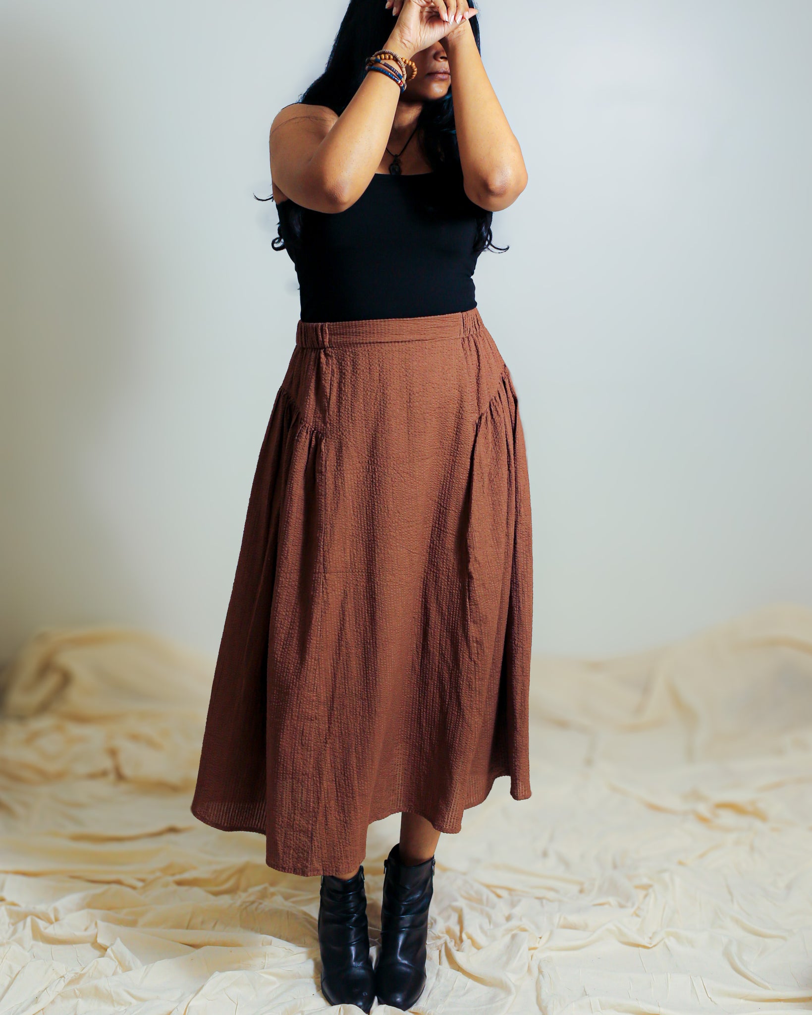 Model wearing a brown cotton skirt styled with a fitted black top and boots.