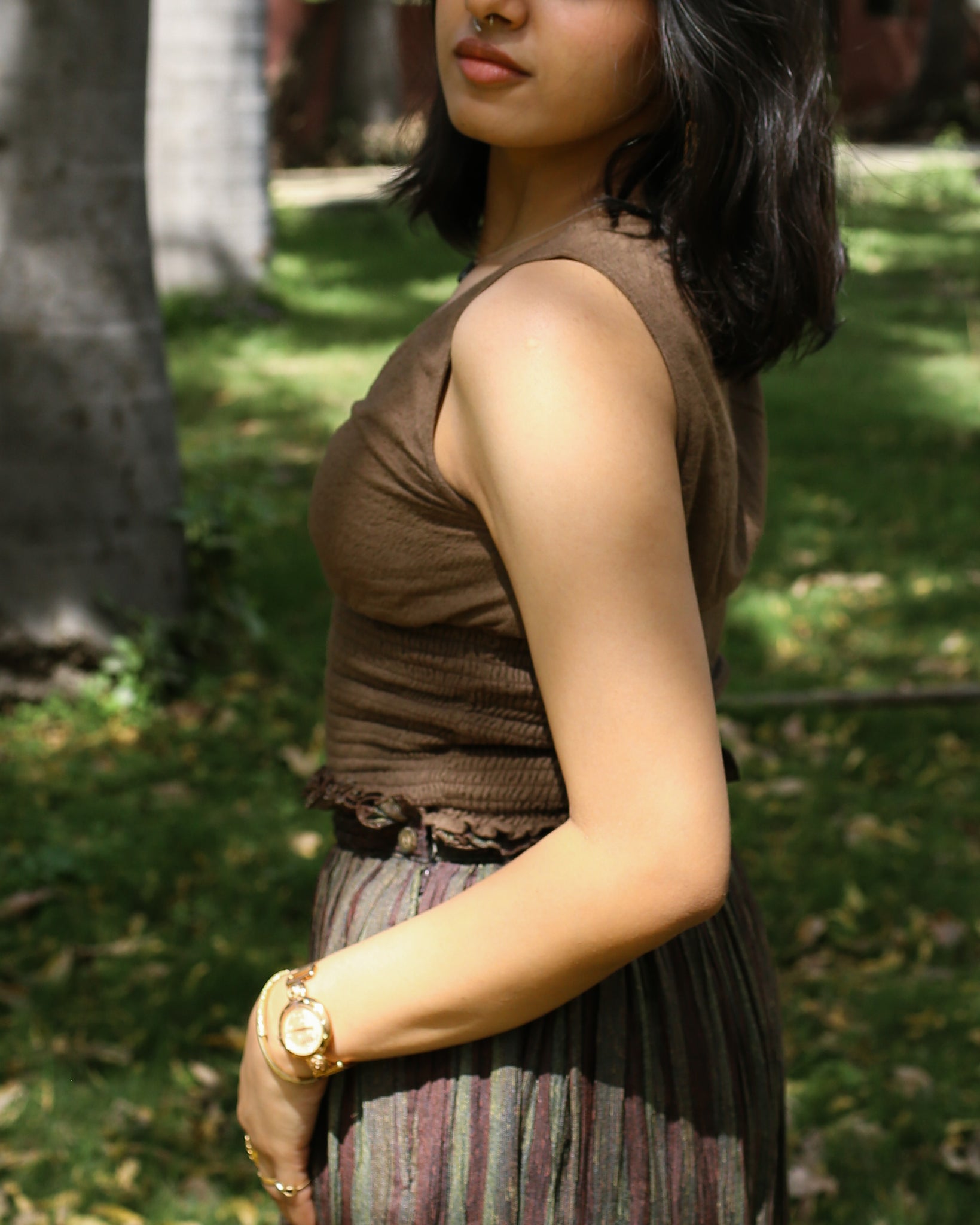 Woman in sleeveless cinch top walking in shade, ideal summer wear with earthy textures.