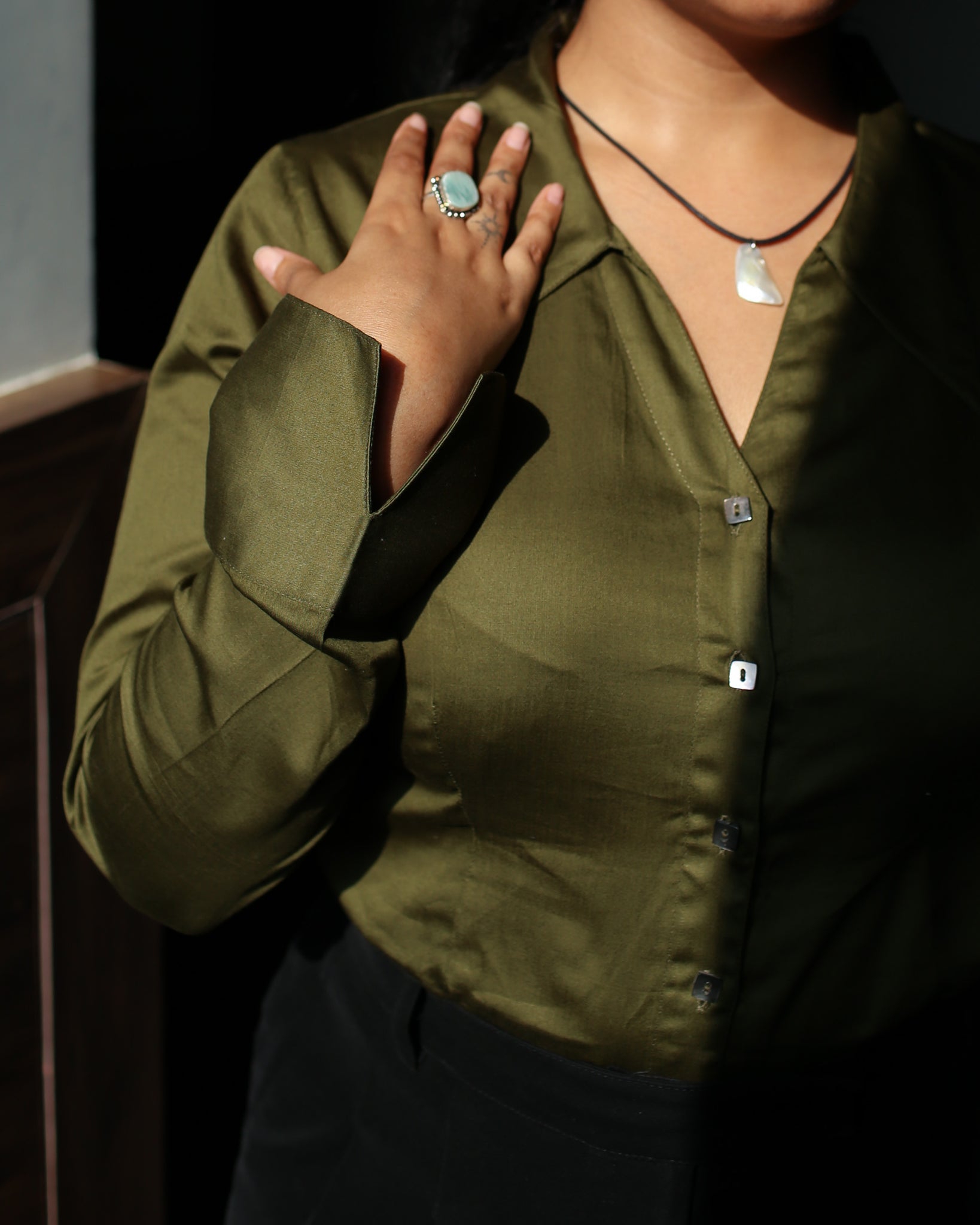 Close-up of mother of pearl square buttons on olive green fitted satin shirt with sharp collar.