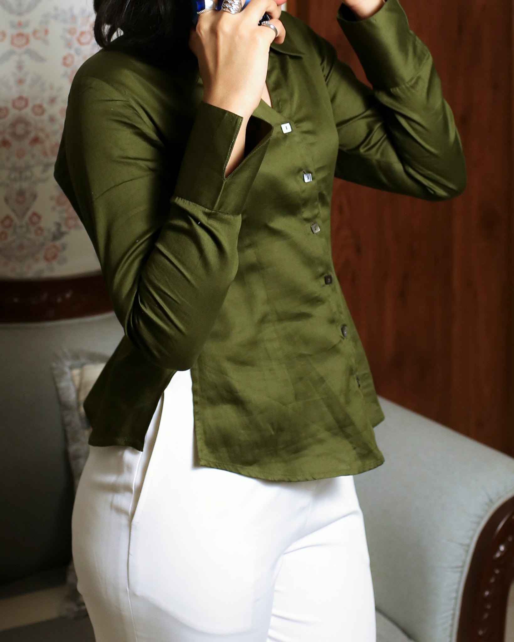 Close-up of mother of pearl square buttons on olive green fitted satin shirt with sharp collar.