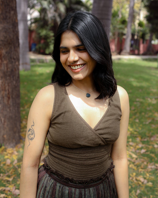 Woman wearing mossbark green cotton cinch top with V-neck and smocked waist, smiling in sunlight.