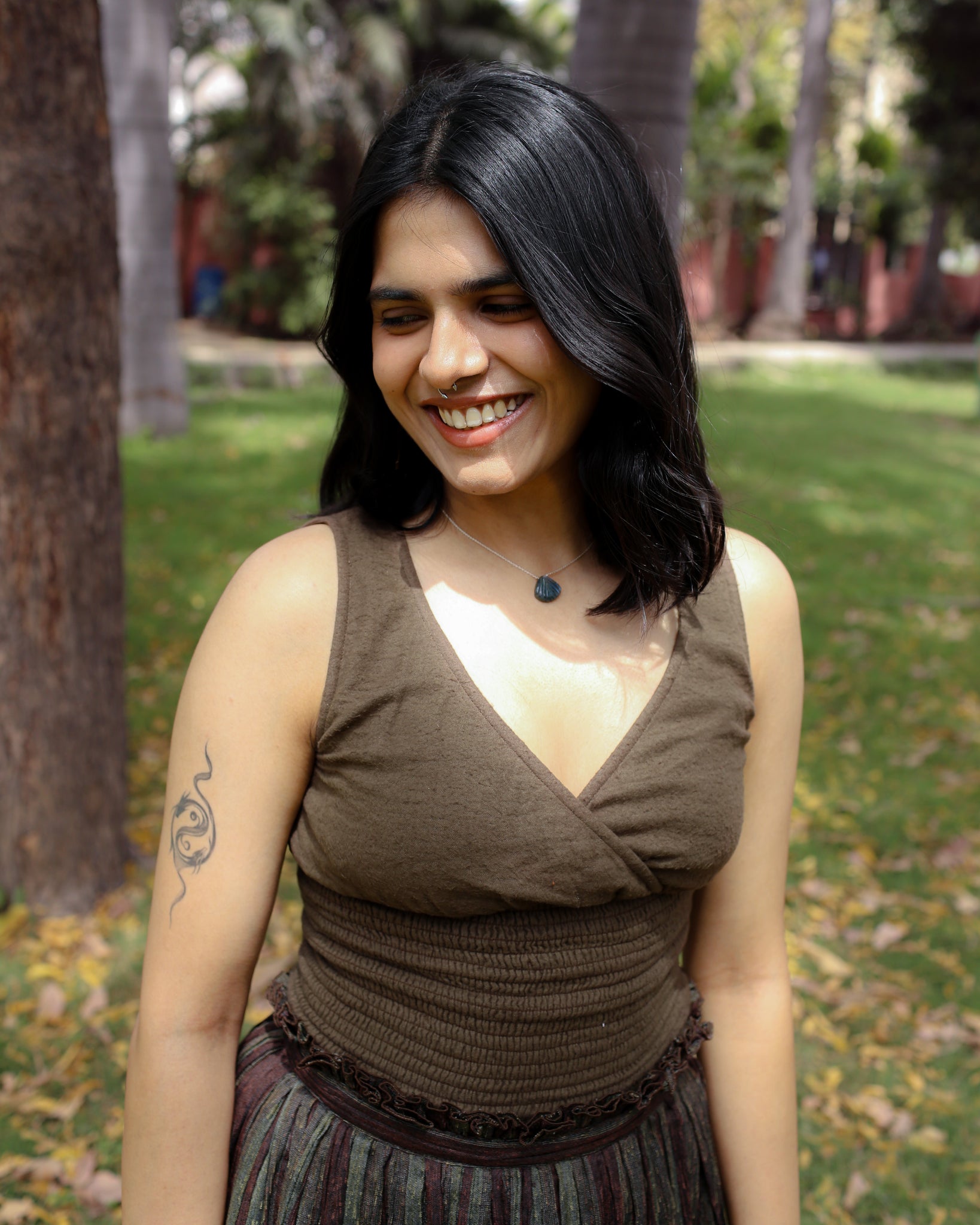 Woman wearing mossbark green cotton cinch top with V-neck and smocked waist, smiling in sunlight.