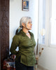 Side view of sculpted olive green satin cotton shirt on older woman, showing relaxed fit and sleeve length.