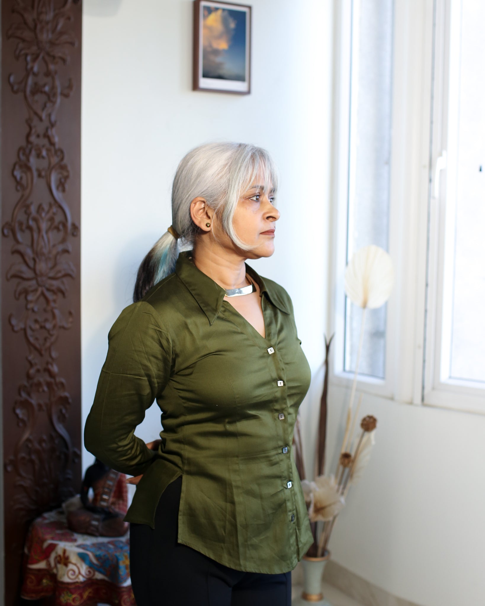 Side view of sculpted olive green satin cotton shirt on older woman, showing relaxed fit and sleeve length.