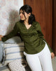 Woman in green satin shirt seated with arm on couch, showing soft sheen of cotton satin fabric.