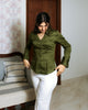 Woman wearing fitted olive green cotton satin shirt with sharp collar, front view, paired with white pants.
