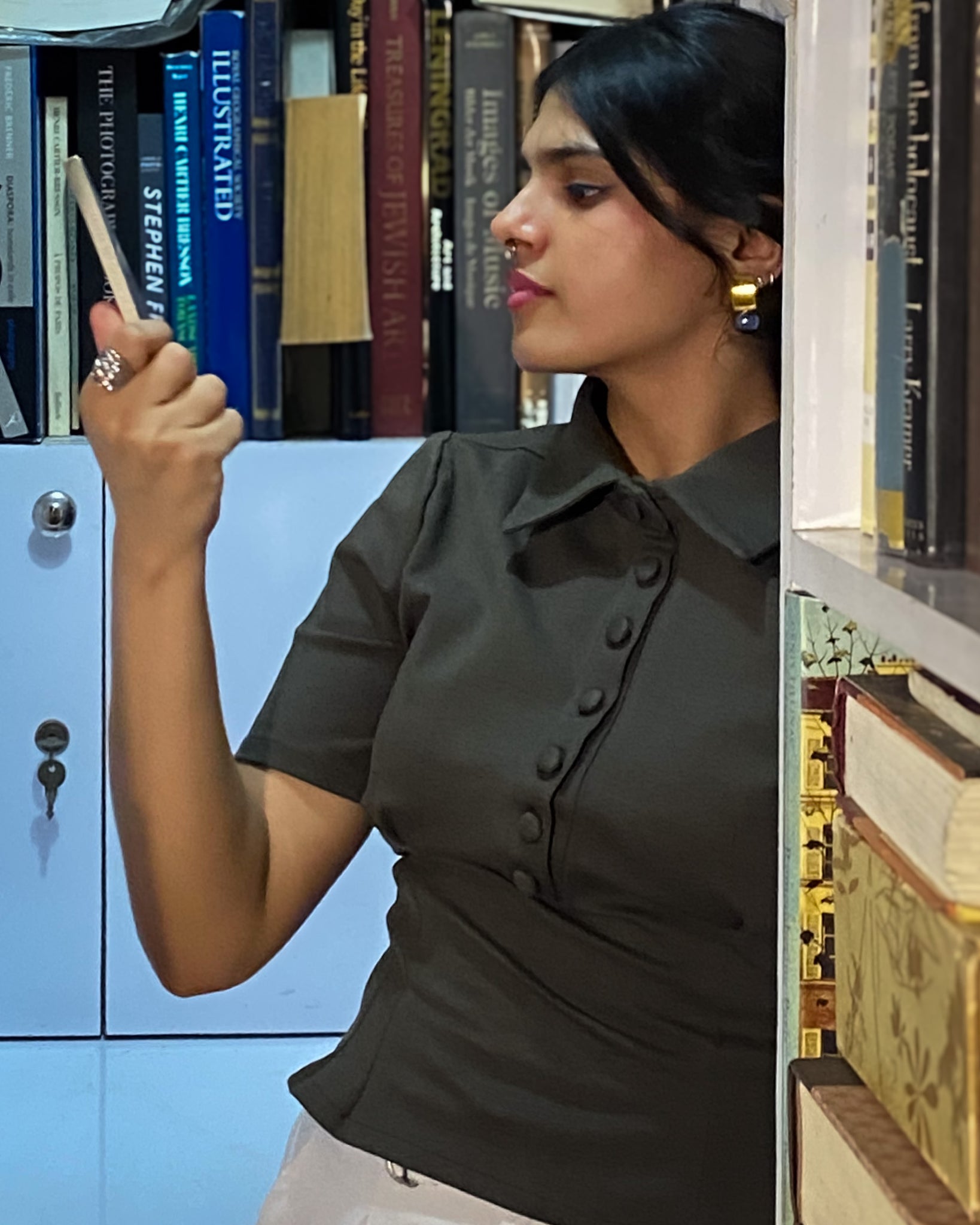 Woman in green sculpted polo top paired with trouser standing near bookshelf.