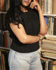 Boxy hand-knitted black wool sweater in 100% pure wool with braided knit detailing on the front standing in library.