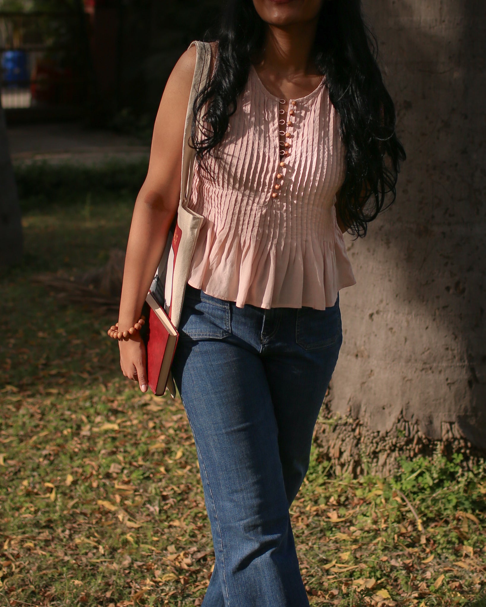 Side view of sleeveless cotton pleated top with wooden buttons and soft peplum flare, lightweight summer wear