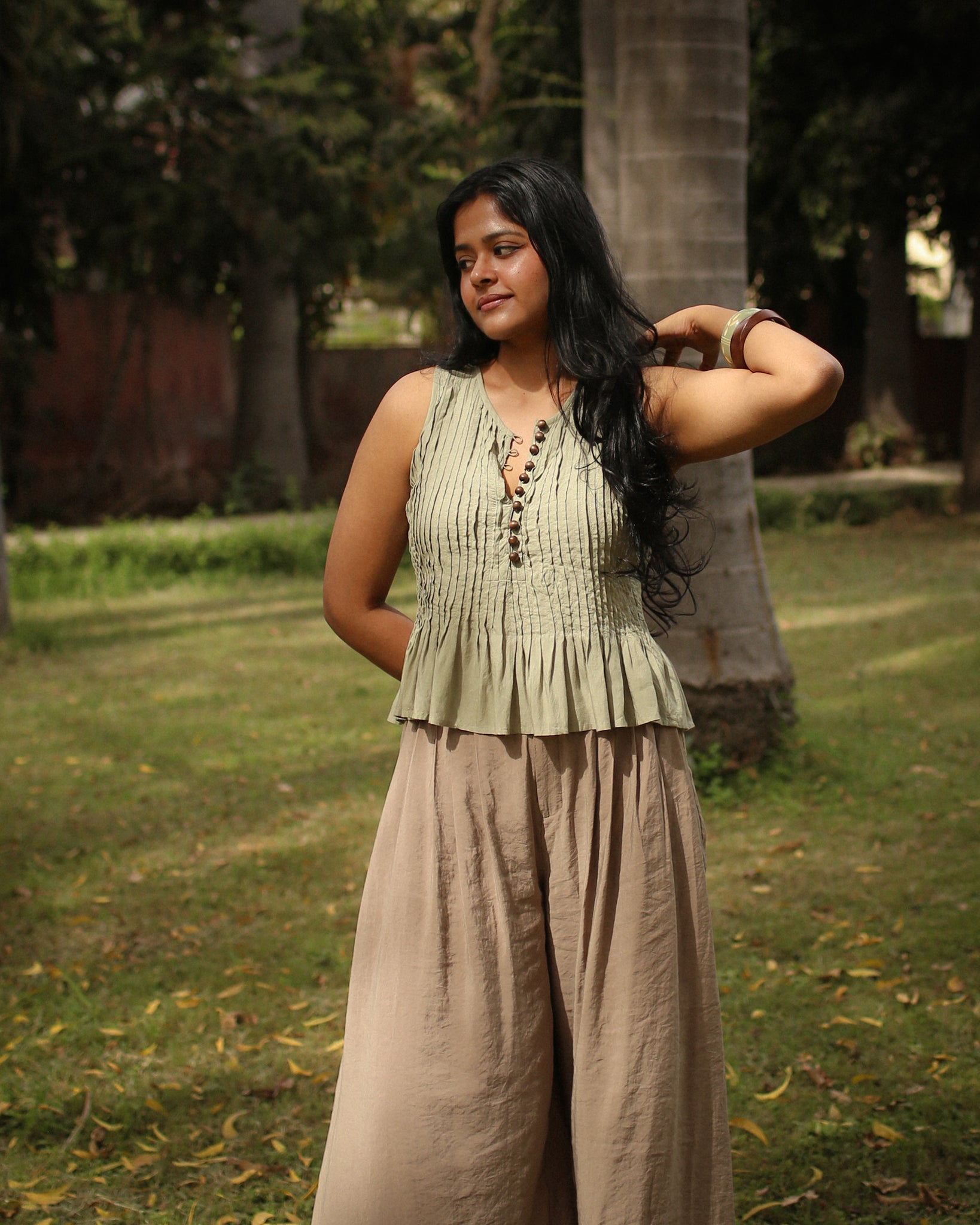 Front fit of sage cotton pleated top with wooden buttons and soft peplum flare, minimal summer style